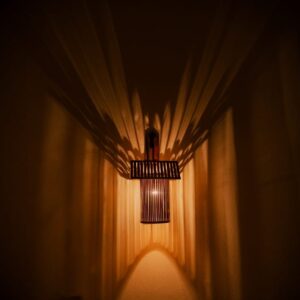 Handcrafted house-shaped bamboo wall lamp casting a warm glow, perfect for rustic home and cafe decor